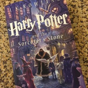 Portada de 'Harry Potter y la piedra filosofal' de J.K. Rowling, que muestra a Harry Potter con una túnica de mago volando en una escoba, con el castillo de Hogwarts y una snitch dorada en el fondo