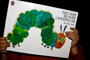 Portada de 'La oruga muy hambrienta' de Eric Carle, que presenta una oruga colorida con cuerpo verde y cabeza roja sobre un fondo blanco.