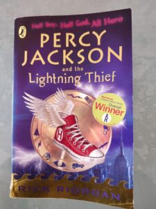 Portada de 'Percy Jackson y el ladrón del rayo' de Rick Riordan, que presenta un solo zapato alado contra un cielo oscuro y tormentoso con rayos.