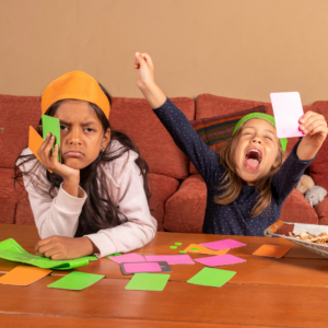 Dos niños jugando a las cartas. Uno de ellos celebra con entusiasmo mientras el otro se ve molesto porque perdió